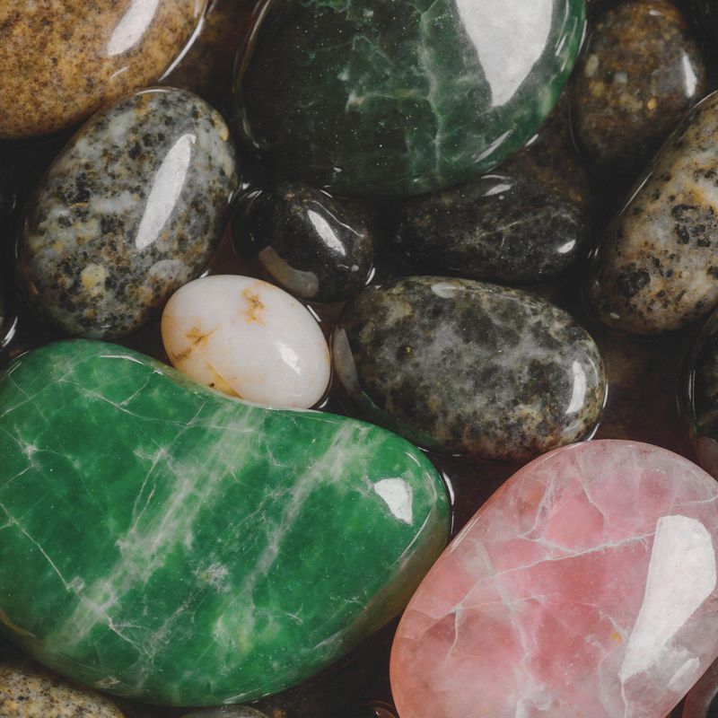 A collection of polished semi-precious stones in green, pink and dark tones.